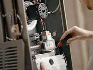 Furnace repair technician inspecting internal components and wiring in Greenville, NC