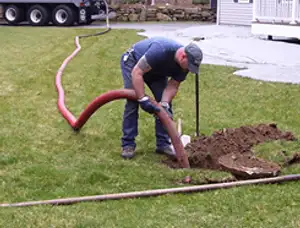 Septic pumping technician servicing a residential septic tank with a vacuum hose in Greenville, NC