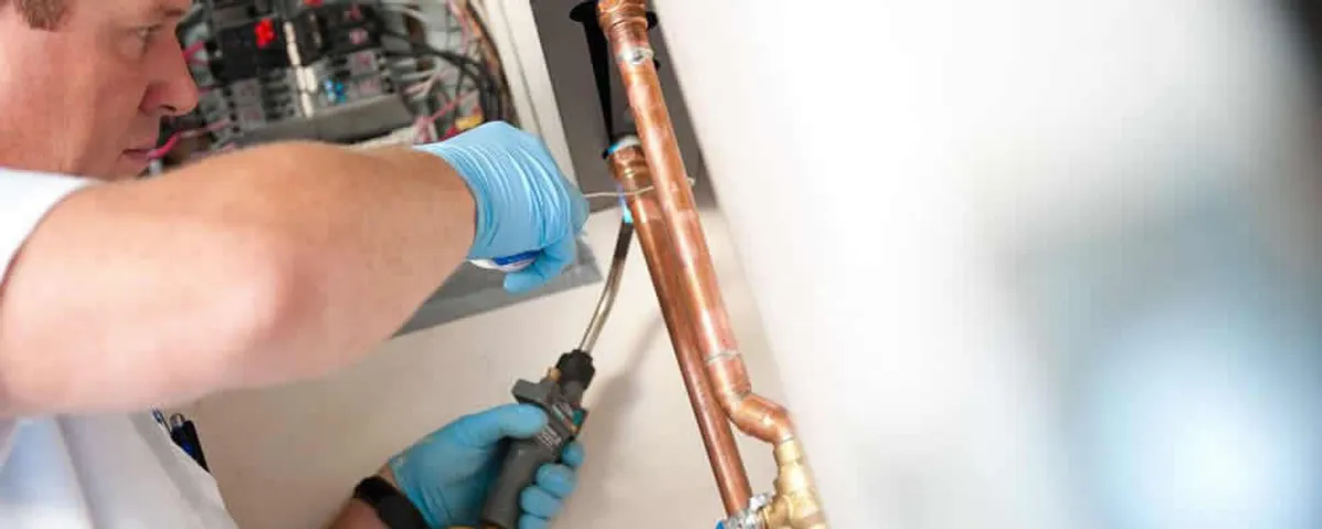 Water heater repair technician testing copper pipe connections and controls in Greenville, NC